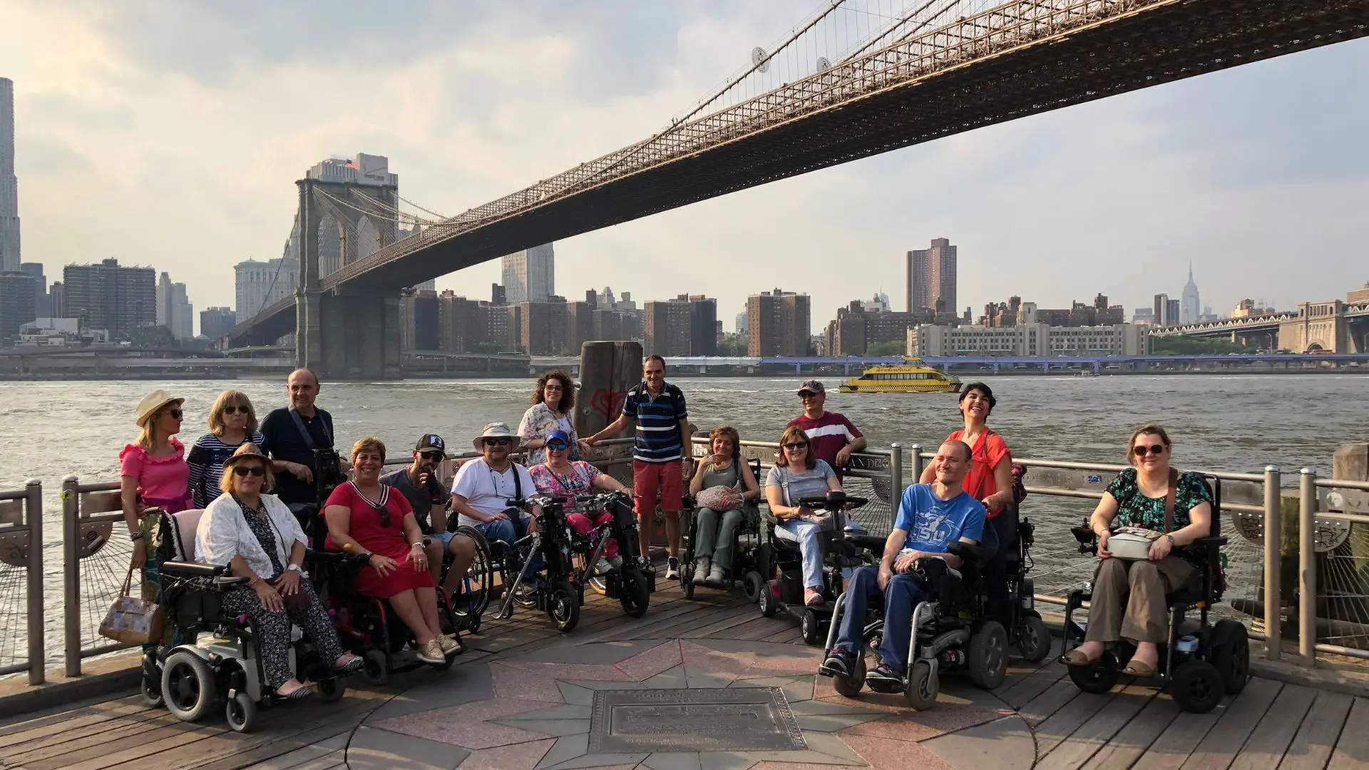 Un grupo de usuarios de silla de ruedas en un viaje en grupo adaptado a Nueva York. Al fondo se ve el puente de Brooklyn