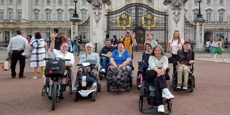 Un grupo de usuarios de silla de ruedas en un viaje adaptado para personas con discapacidad a Londres frente al palacio de Buckingham.