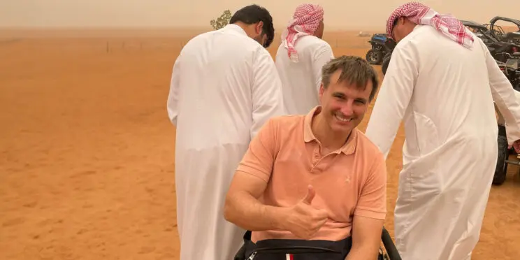 Un usuario de silla de ruedas en el desierto de Dubai ayudado por otras personas en la arena