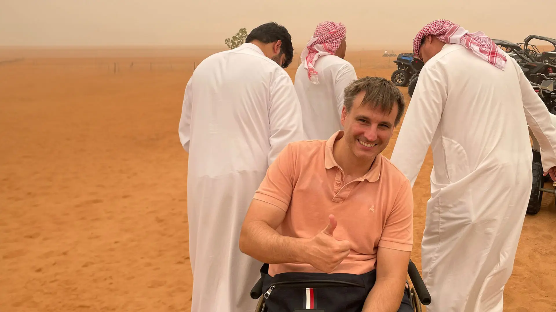 Un usuario de silla de ruedas en el desierto de Dubai ayudado por otras personas en la arena