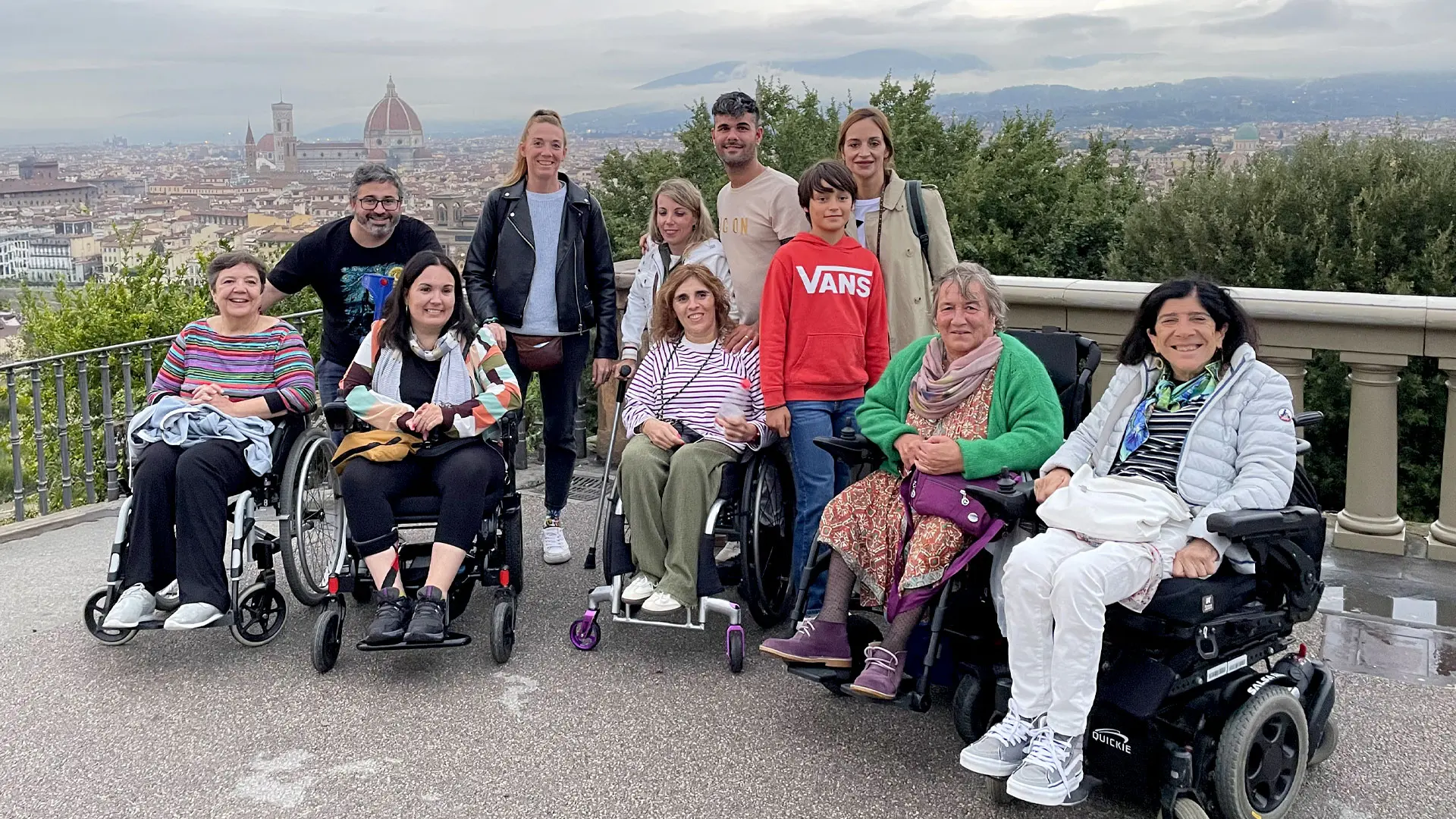 Un grupo de viajeros y viajeras usuarias de silla de ruedas en un viaje adaptado en grupo a Florencia. Al fondo se ve la ciudad de Florencia y la cúpula de la catedral.
