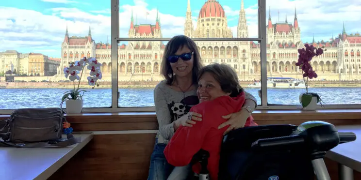 2 personas con discapacidad disfrutando de un crucero accesible por el danubio con el Parlamento de Budapest en el fondo