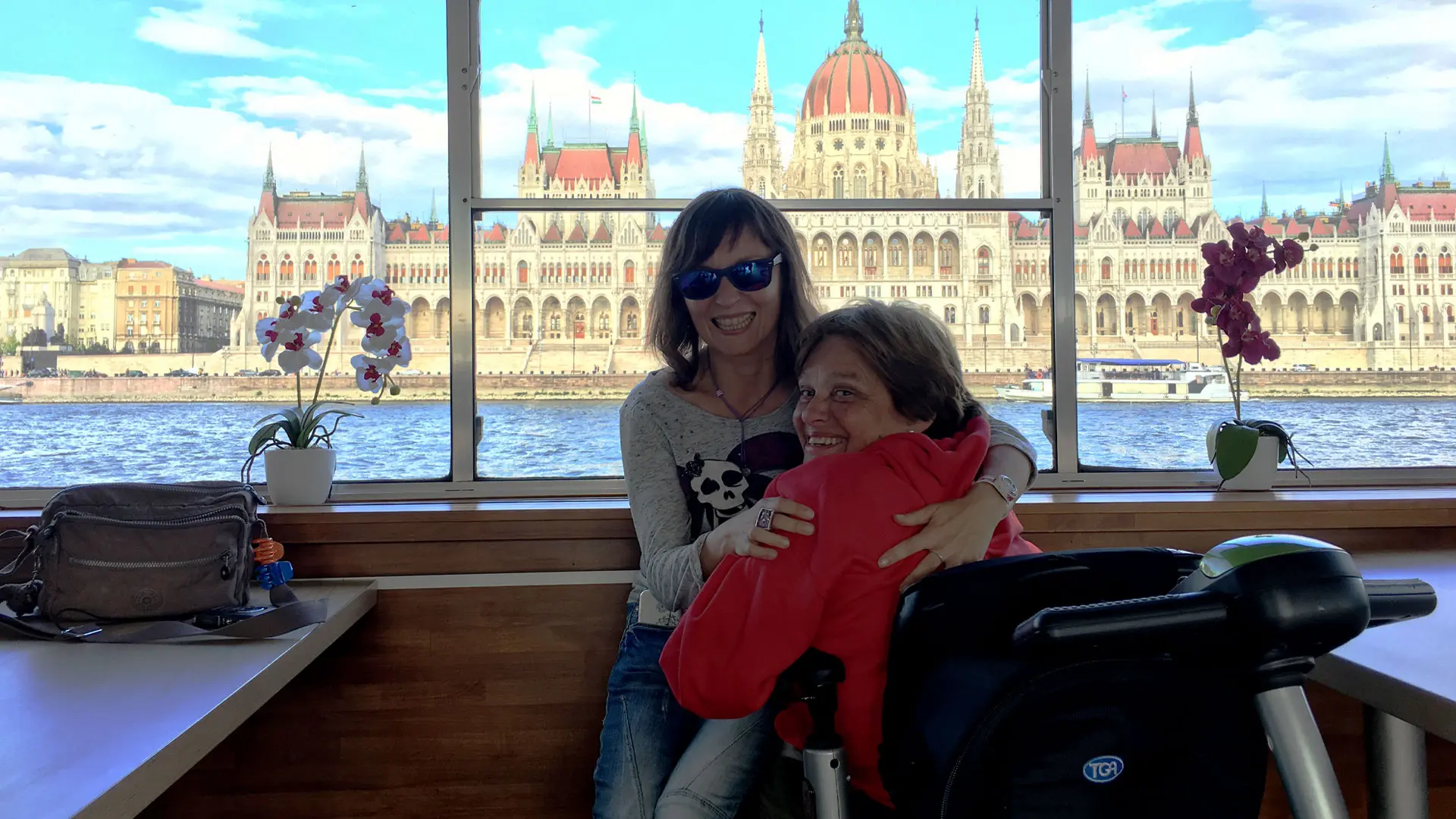 2 personas con discapacidad disfrutando de un crucero accesible por el danubio con el Parlamento de Budapest en el fondo