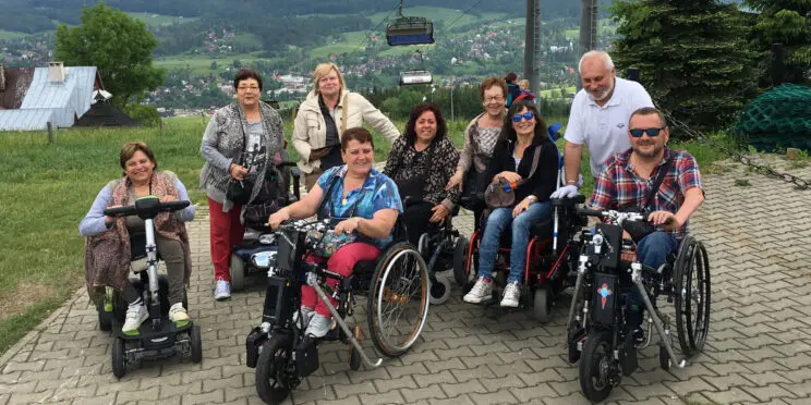 Grupo de usuarios de silla de ruedas en lo alto de una montaña en Zakopane. Detrás de ellos se va la vistas del vaye.