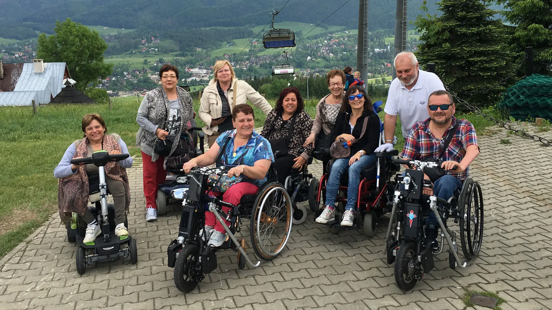 Grupo de usuarios de silla de ruedas en lo alto de una montaña en Zakopane. Detrás de ellos se va la vistas del vaye.