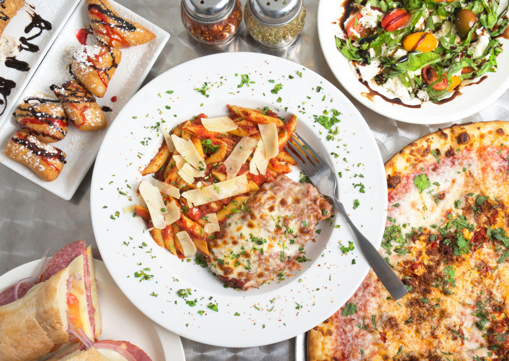 Italia accesible Gastronomía sin barreras en Italia accesible. Imagen de un amesa con un plato de pasta al centro, una pizza a su derecha y varios platos de comida en un segundo plano.