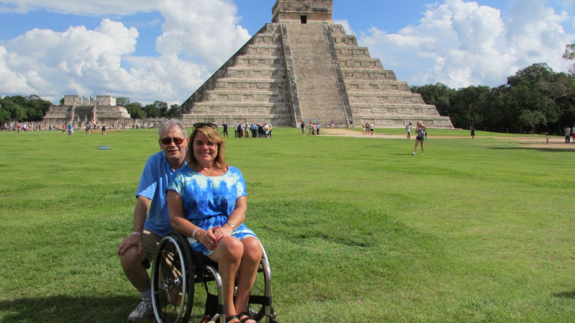 Una pareja viajando por México, ella, usuaria de silla de ruedas, al fondo, la pirámide de Chichén Itzá