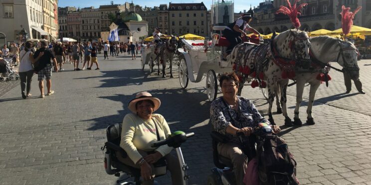 Dos viajeras en silla de ruedas disfrutando de Cracovia con un carruaje detrás