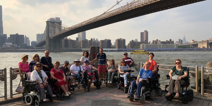 Un grupo de usuarios de silla de ruedas en un viaje en grupo adaptado a Nueva York. Al fondo se ve el puente de Brooklyn