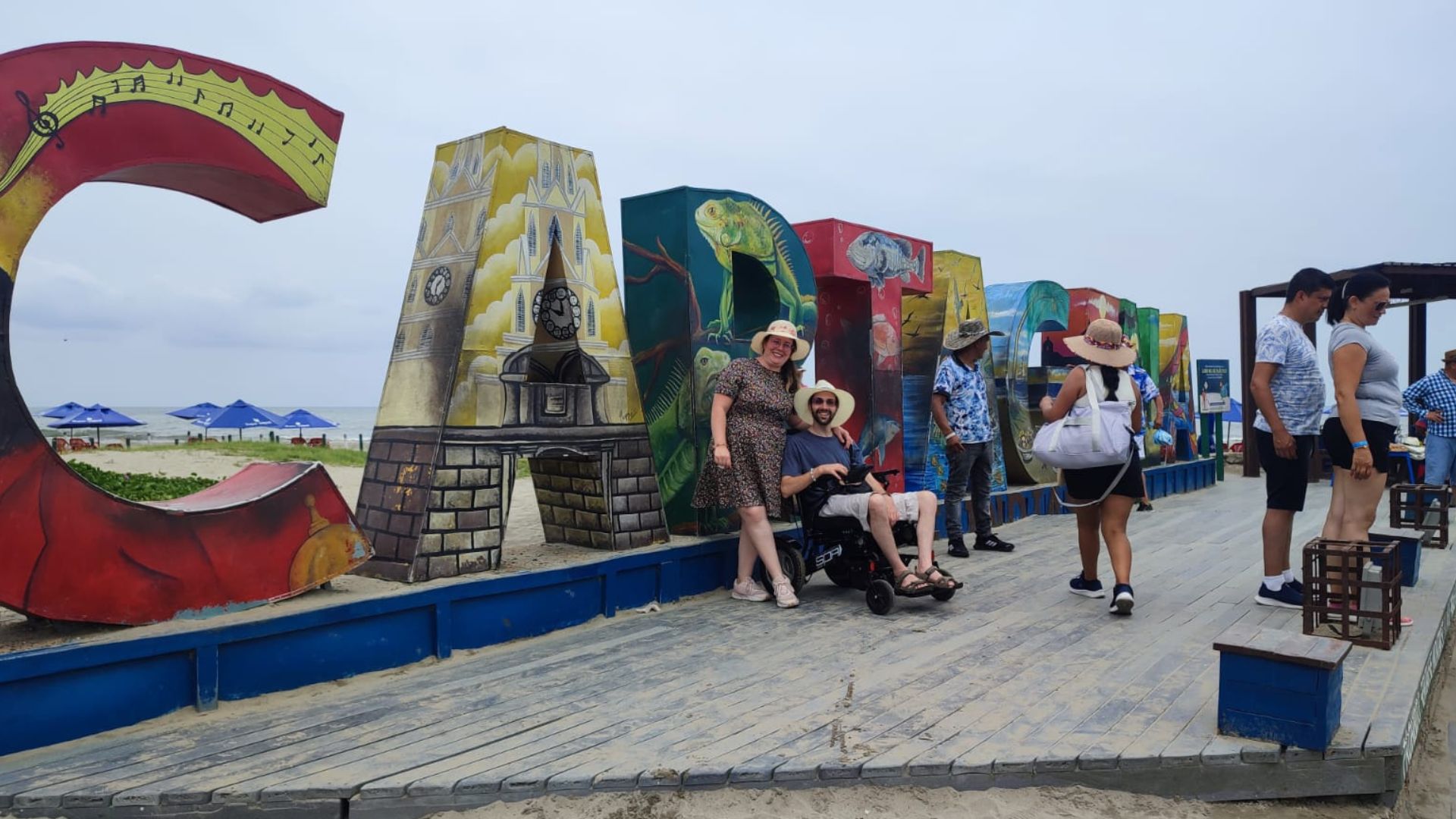 Una pareja, él usuario de silla de ruedas, en un viaje adaptado a Colombia, frente al cartel turístico de Cartagena