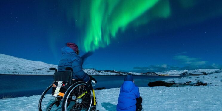 Una madre usuaria de silla de ruedas junto a su hijo disfrutando de las auroras boreales en un viaje en silla de ruedas a Tromso