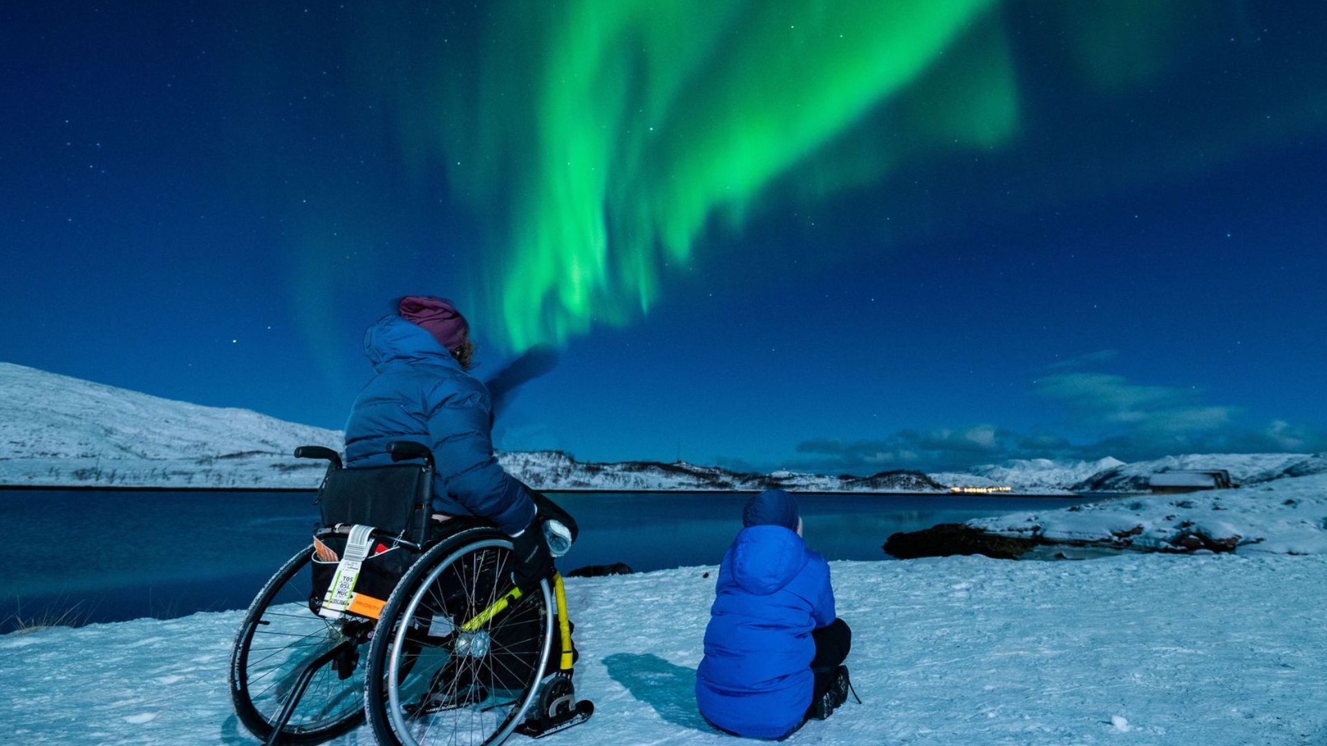 Una madre usuaria de silla de ruedas junto a su hijo disfrutando de las auroras boreales en un viaje en silla de ruedas a Tromso