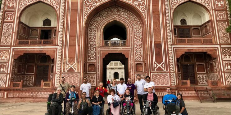 Grupo de viajeros en silla de ruedas en un viaje adaptado a la India posando frente a la puerta del Fuerte Rojo.