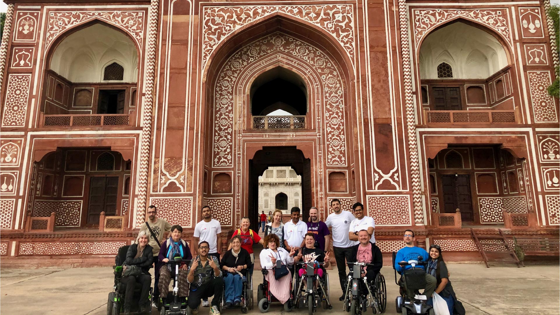 Grupo de viajeros en silla de ruedas en un viaje adaptado a la India posando frente a la puerta del Fuerte Rojo.