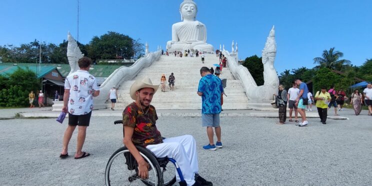 Usuario de silla de ruedas en un templo en Tailandia, al fondo se puede ver una estatua de un Buda blanco