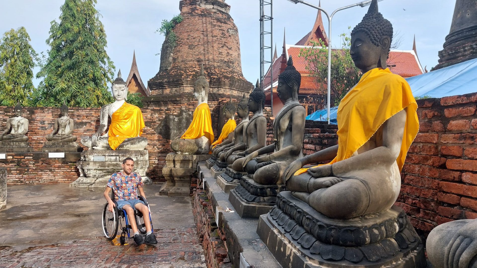 Un usuario de silla de ruedas en un templo en Tailandia. En la imágen se lo ve en un espacio rodeado de estatuas de budas con trajes dorados.