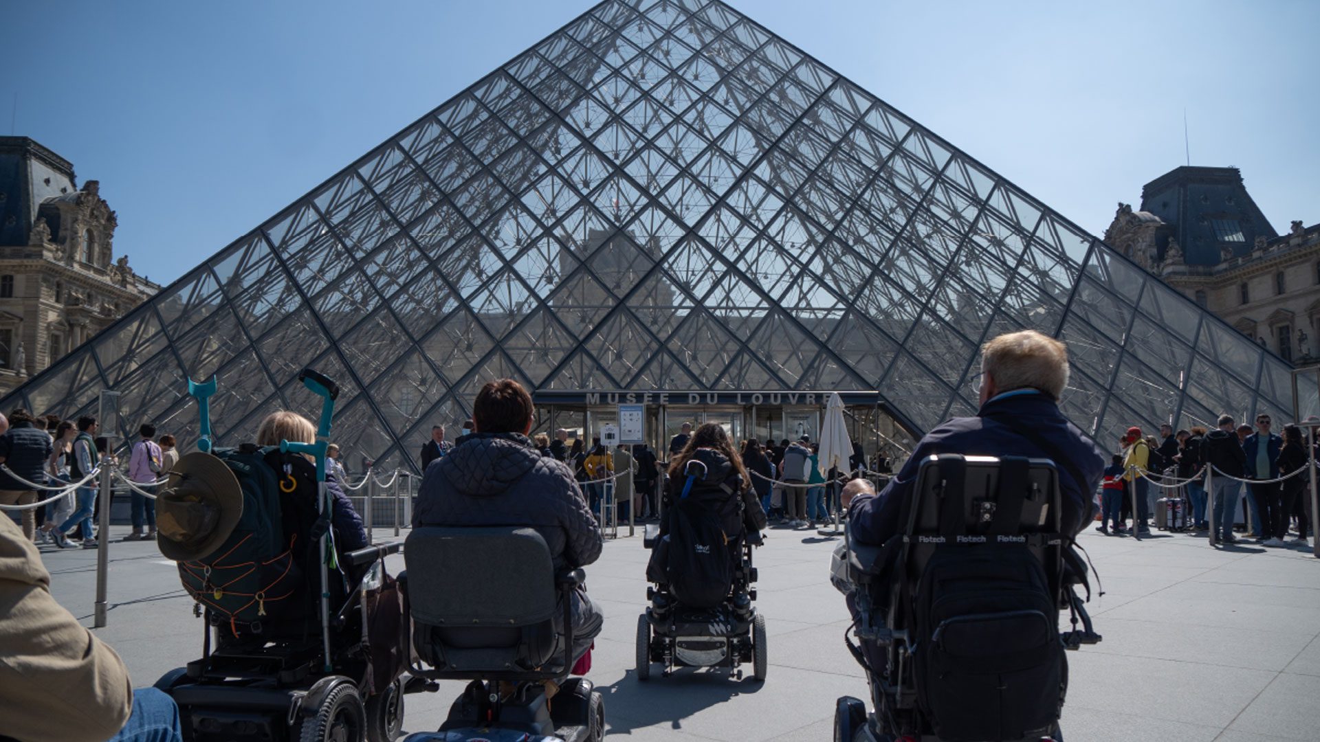 Un grupo de usuarios de silla de ruedas viendo la entrada al museo del Louvre