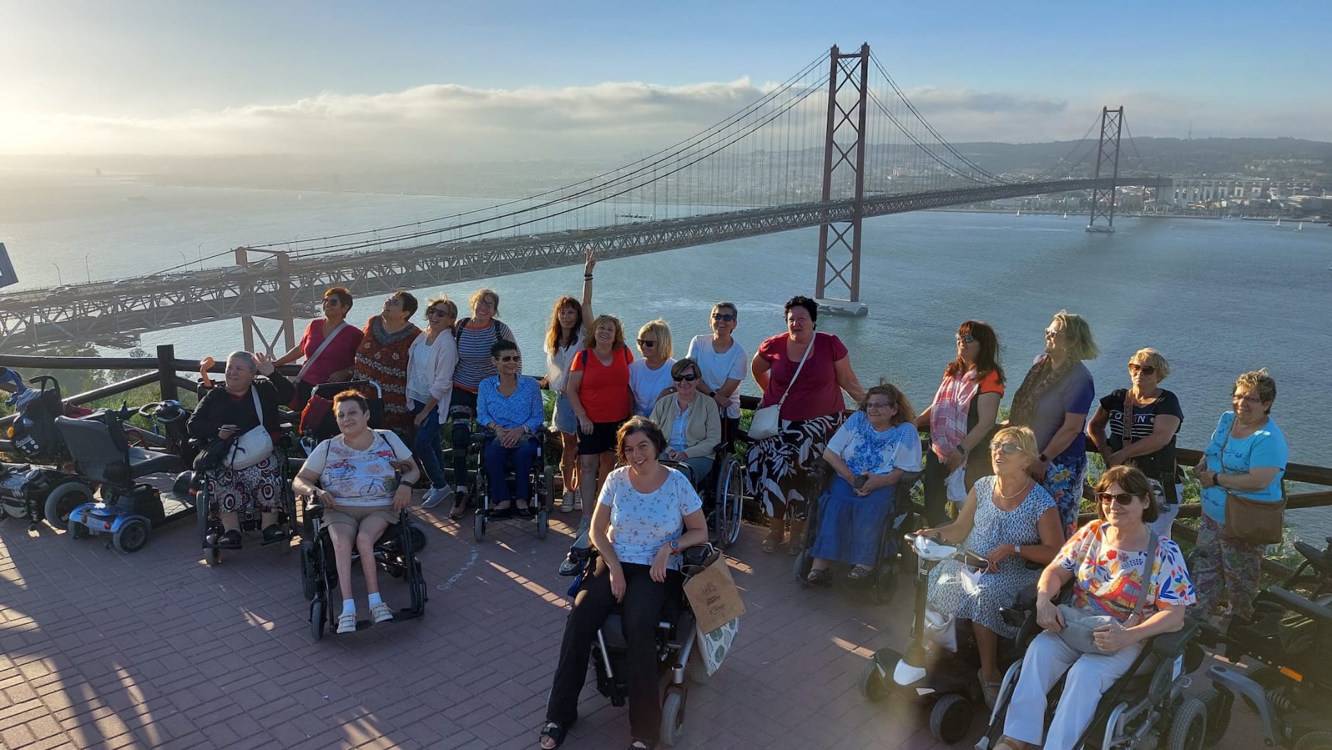 Un grupo de personas usuarias de silla de ruedas en un mirador. Al fondo, se ve el puente de Lisboa.