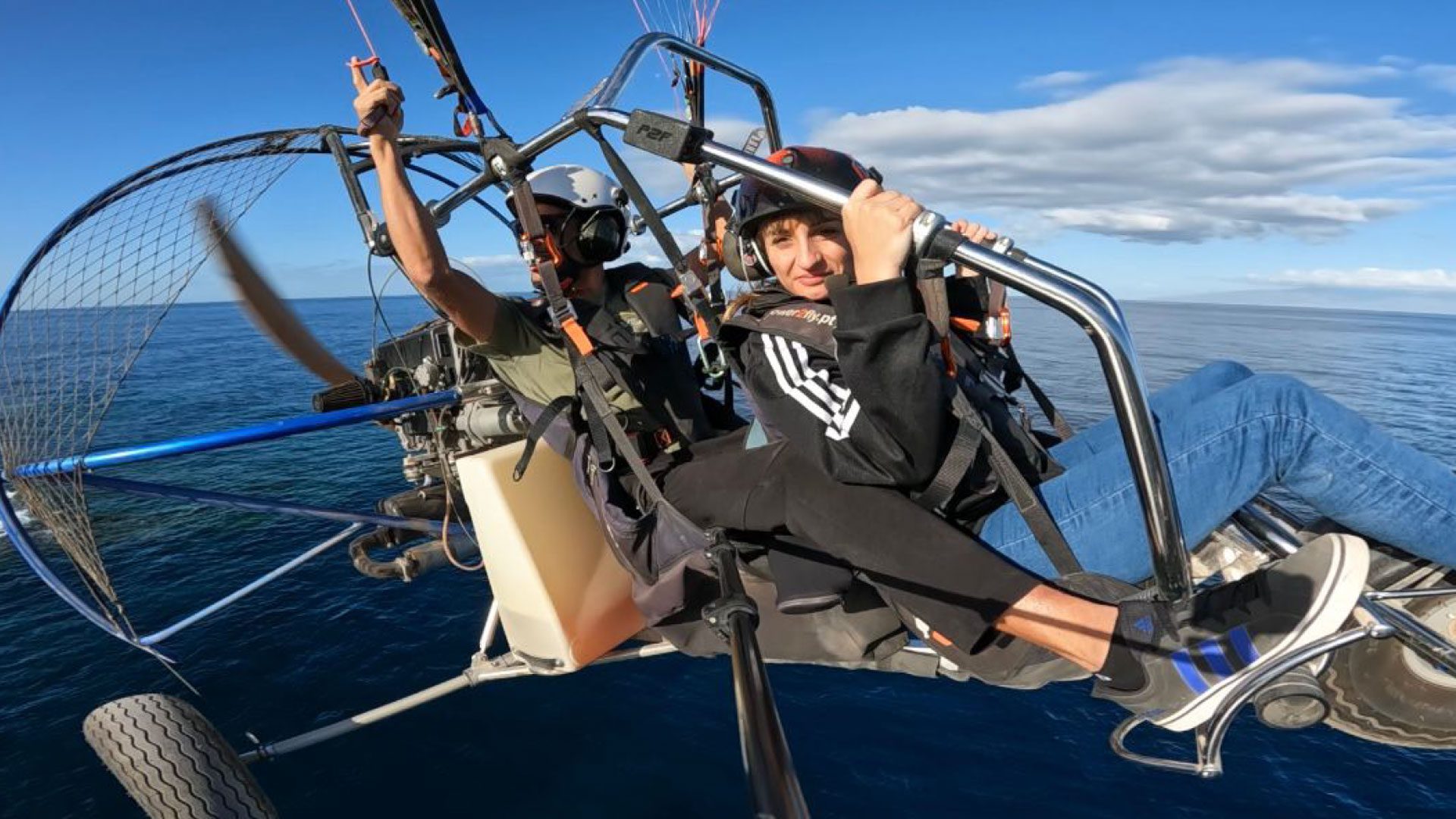 Una persona usuaria de silla de ruedas junto a un instructor realizando la actividad de parapente