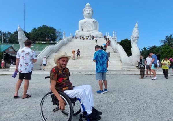 Usuario de silla de ruedas en un templo en Tailandia, al fondo se puede ver una estatua de un Buda blanco