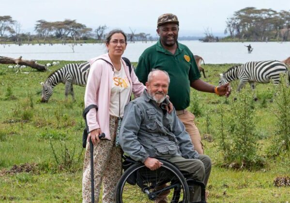 Una persona con discapacidad en un viaje adaptado a Kenia junto a su esposa y un guía en un tour accesible en un safari