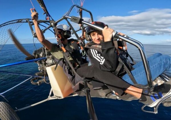 Una persona usuaria de silla de ruedas junto a un instructor realizando la actividad de parapente