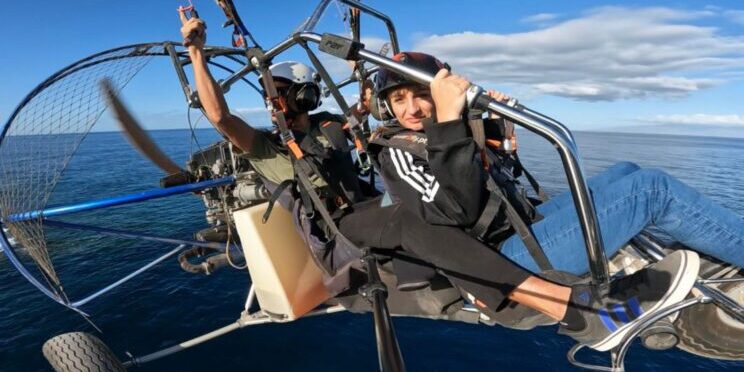 Una persona usuaria de silla de ruedas junto a un instructor realizando la actividad de parapente