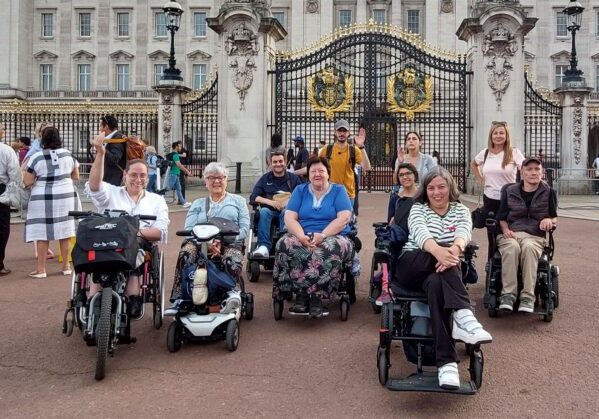 Un grupo de usuarios de silla de ruedas en un viaje adaptado para personas con discapacidad a Londres frente al palacio de Buckingham.