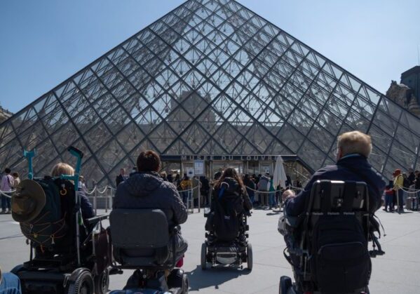 Un grupo de usuarios de silla de ruedas viendo la entrada al museo del Louvre