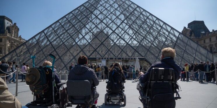 Un grupo de usuarios de silla de ruedas viendo la entrada al museo del Louvre