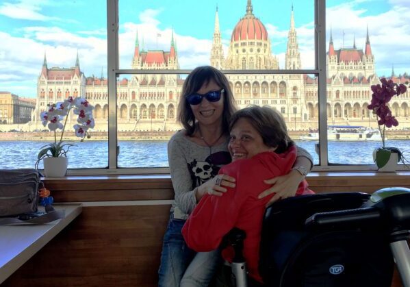 2 personas con discapacidad disfrutando de un crucero accesible por el danubio con el Parlamento de Budapest en el fondo