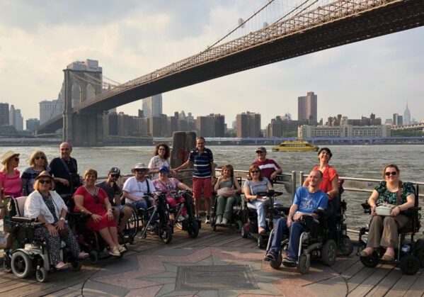 Un grupo de usuarios de silla de ruedas en un viaje en grupo adaptado a Nueva York. Al fondo se ve el puente de Brooklyn