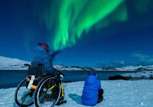 Una madre usuaria de silla de ruedas junto a su hijo disfrutando de las auroras boreales en un viaje en silla de ruedas a Tromso