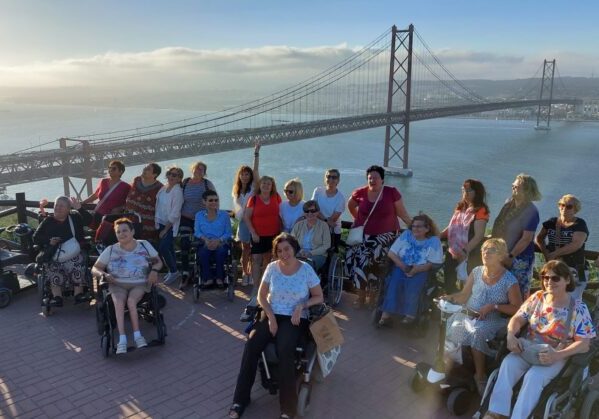 Un grupo de personas usuarias de silla de ruedas en un mirador. Al fondo, se ve el puente de Lisboa.