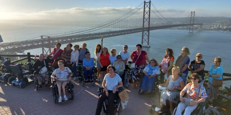 Un grupo de personas usuarias de silla de ruedas en un mirador. Al fondo, se ve el puente de Lisboa.