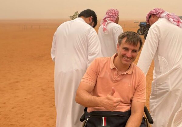 Un usuario de silla de ruedas en el desierto de Dubai ayudado por otras personas en la arena