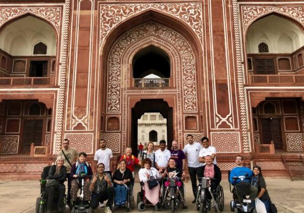 Grupo de viajeros en silla de ruedas en un viaje adaptado a la India posando frente a la puerta del Fuerte Rojo.