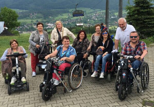 Grupo de usuarios de silla de ruedas en lo alto de una montaña en Zakopane. Detrás de ellos se va la vistas del vaye.