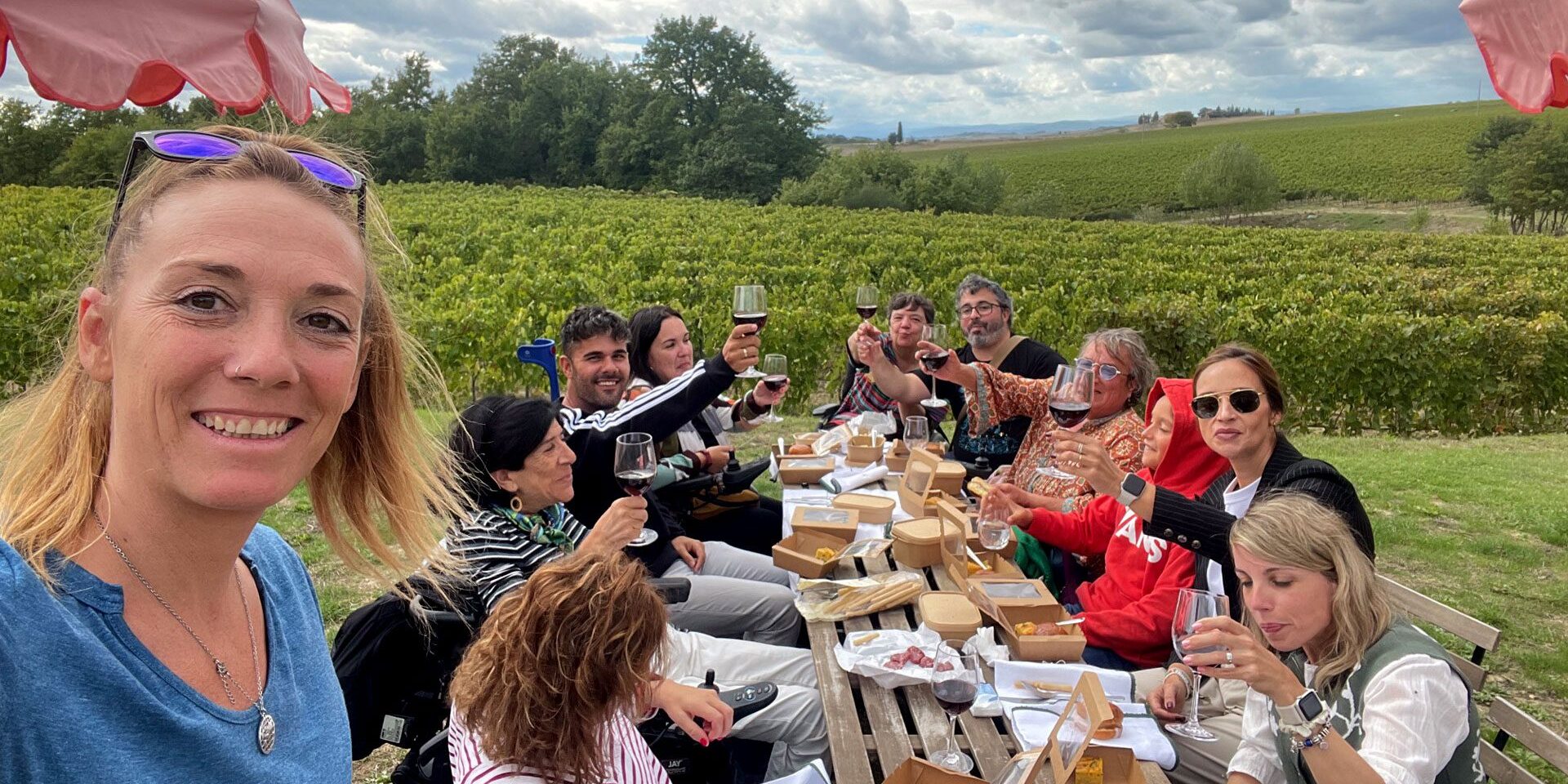 Viajar a Italia en silla de ruedas Imagen de un grupo de personas entre ellos, algunos usuarios de silla de ruedas, brindando y comiendo junto a un viñedo en la Tostaca.