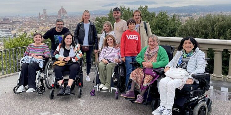 Un grupo de viajeros y viajeras usuarias de silla de ruedas en un viaje adaptado en grupo a Florencia. Al fondo se ve la ciudad de Florencia y la cúpula de la catedral.